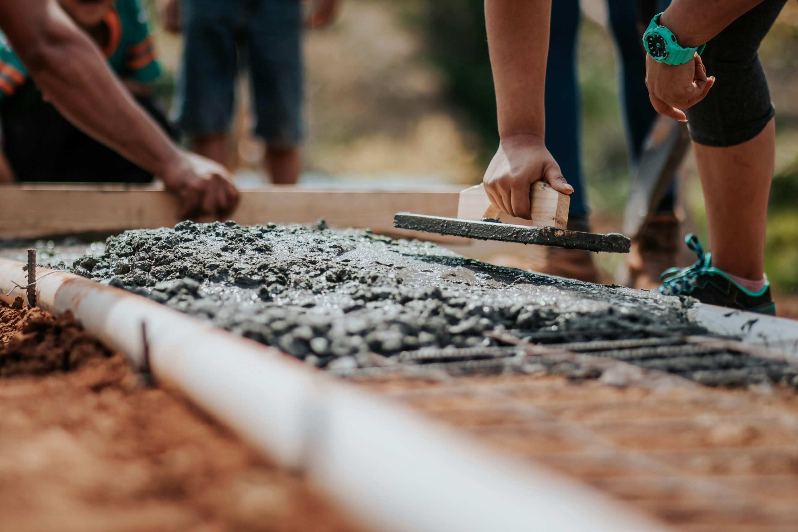 pexels-photo-2219024-2219024 Construction workers leveling fresh cement on a sunny day at an outdoor site.